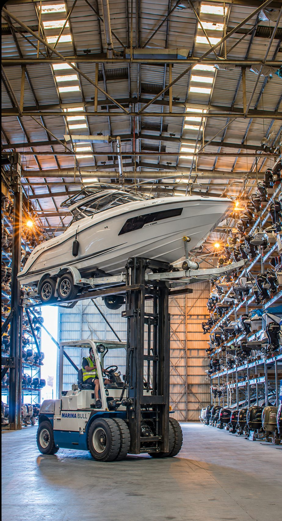 Rendering of the Gold Key Boathouse interior aisle — a marine forklift carrying a boat on its own trailer between four-high racks, with RVs on the ground floor